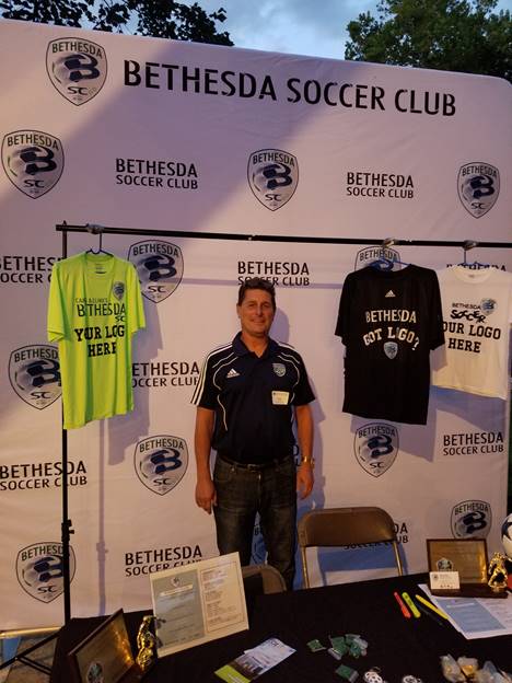 (l:r) Bethesda Soccer Club’s Executive Director Brad Roos, displays his new backdrop at the Gaithersburg-Germantown Chamber non-profit showcase & membership picnic at Smokey Glen Farm. They are a select youth soccer club for ages 7-19. Learn more about them at www.bethesdasoccer.org.  (Photo credit –Laura Rowles, Director of Marketing, Gaithersburg-Germantown Chamber)